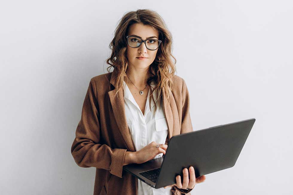 A Google Ads Specialist, a young woman with slightly curled honey brown hair. She holds a laptop and looks purposefully into the camera.